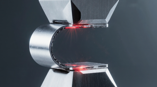 Metals testing and failure analysis – close‑up of tensile test on metal specimen with laser measurement in materials testing laboratory